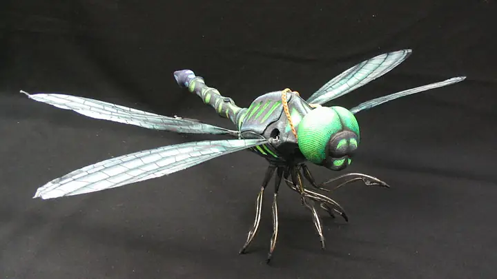 Mechanical dragonfly with veined wings and a green head on a black cloth